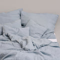Leinenkissenbezug blau in verschiedenen Größen auf einem Bett, geeignet für ein gemütliches Schlafzimmer.