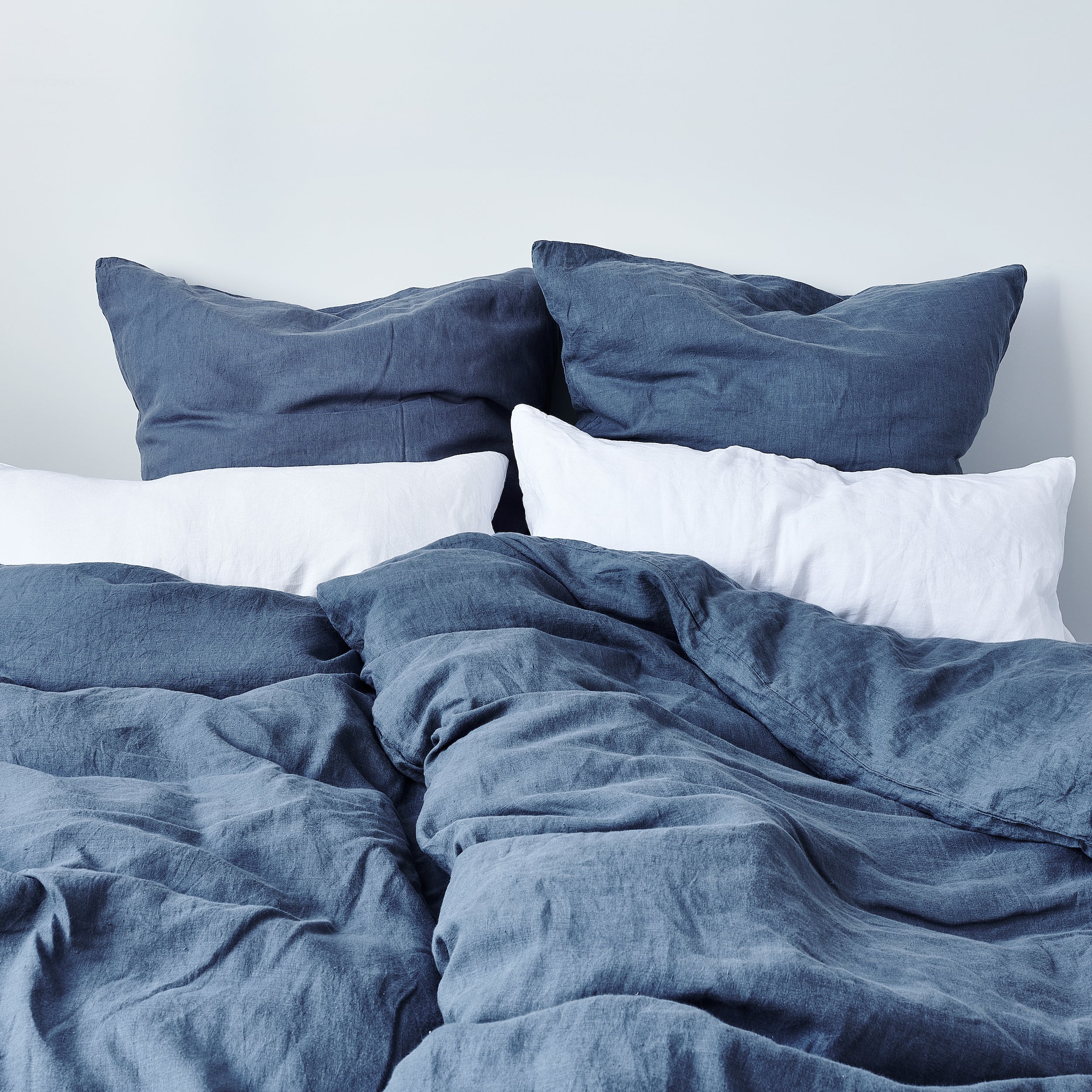 Leinen-Kissenbezug Atlantikblau auf einem Bett mit weißen und grauen Kissen und einer zerknitterten Bettdecke.