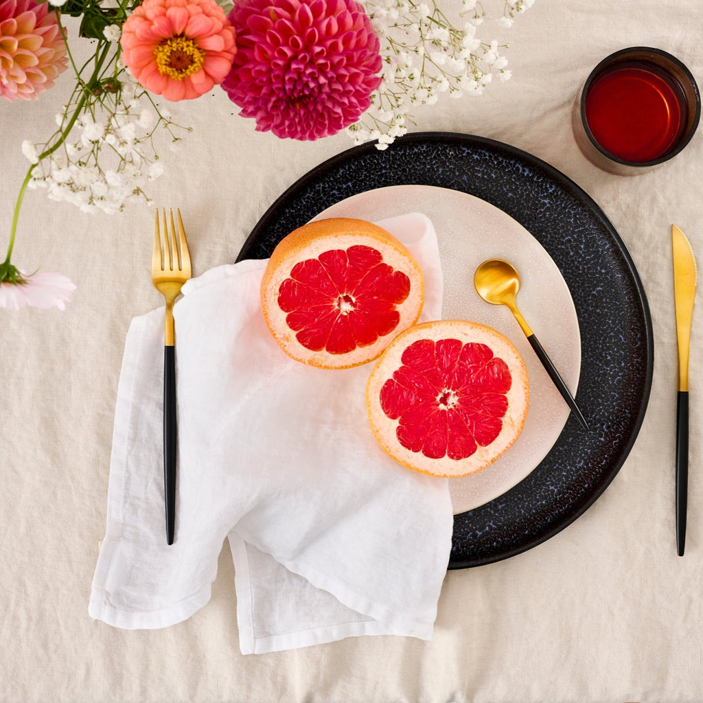 Leinen-Servietten Alpinweiß, 4 Stück auf einem Tisch mit Grapefruit und Blumenarrangement.